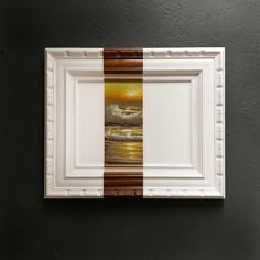 a white frame hanging on the wall with a brown and white painting in front of it