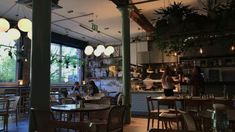 people sitting at tables in a restaurant with lots of plants hanging from the ceiling and windows