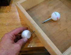 a person is holding a golf ball in front of a hole on a wooden table