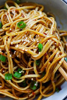 a bowl full of noodles with chopsticks in it and sesame seeds on the side