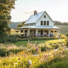 a white house sitting in the middle of a lush green field with flowers around it