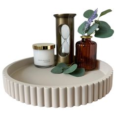 a white tray with two vases and a candle on it next to some green leaves