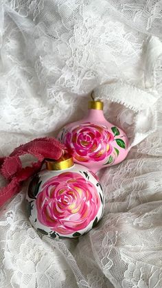 two pink ornaments sitting on top of a white lace covered table cloth next to each other