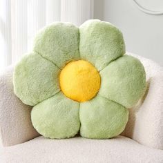 a green flower shaped pillow sitting on top of a white chair next to a window