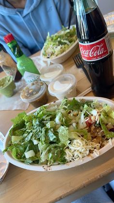 a person sitting at a table with a plate of salad and coke in front of them