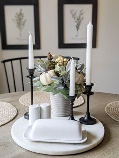 a white plate topped with candles next to a vase filled with flowers and greenery