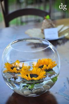 sunflowers and rocks in a glass bowl on a table