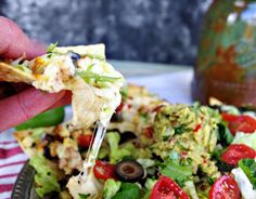 a hand holding a slice of pizza over a salad with olives, tomatoes and lettuce