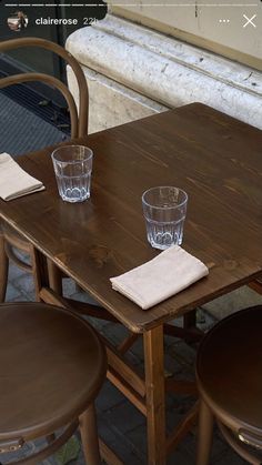 two empty glasses sitting on top of a wooden table next to chairs and a window