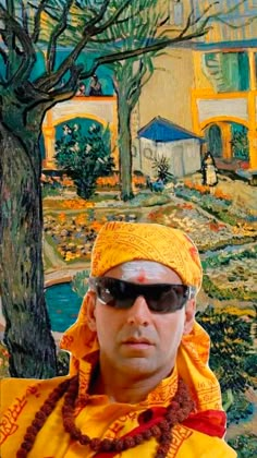 a man wearing sunglasses and a yellow headdress stands in front of a painting