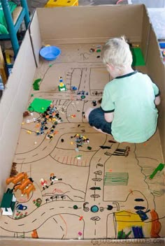 a child playing with lego toys in a cardboard box on the floor next to a toy train track