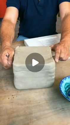 a man is making something out of clay on a wooden table with two bowls and a knife