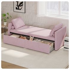 a living room with a pink couch and book shelf under the futon, next to a window