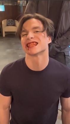 a young man with his mouth open while standing in front of another person wearing a black t - shirt