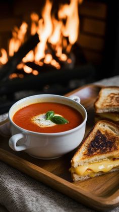 a bowl of soup and grilled cheese sandwiches on a wooden tray in front of a fireplace