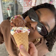 a woman wearing sunglasses is eating an ice cream cone with sprinkles and chocolate