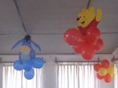 winnie the pooh balloon decorations are hanging from the ceiling in front of two windows