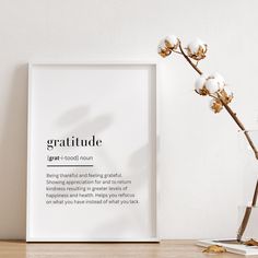 a white framed poster on a table next to a vase with cotton flowers in it