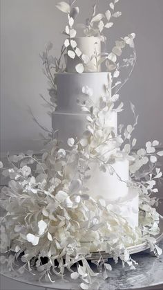 a three tiered white wedding cake with flowers on the side and branches in the middle