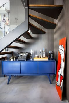 a blue cabinet under a stair case next to a painting