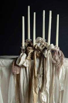 a table topped with lots of white candles and scarves on top of each other