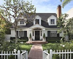 a white house with black shutters on the front and side doors is surrounded by greenery