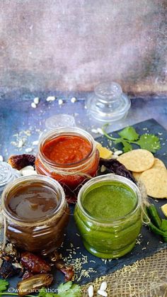 three jars filled with different colored sauces next to crackers and vegetables on a table