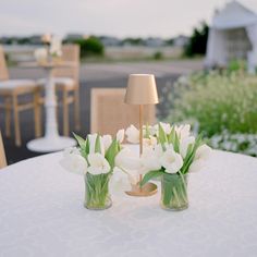 two vases filled with white flowers sitting on top of a table next to a lamp