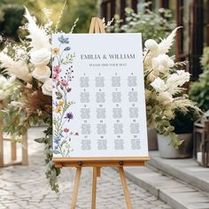 an easel with a seating chart on it and flowers in the background for a wedding ceremony