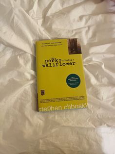 a yellow book sitting on top of a white sheet covered bed next to a pillow