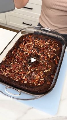 a woman is holding a glass baking dish with pecans in it on a counter