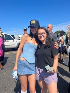 two women standing next to each other in a parking lot with their arms around each other