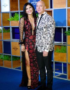 a man and woman standing next to each other in front of a wall with plants