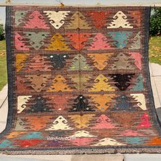 a multicolored rug is hanging on the side of a sidewalk in front of a house