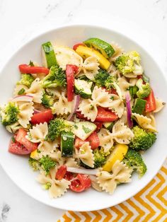 a white bowl filled with pasta salad on top of a yellow and white table cloth