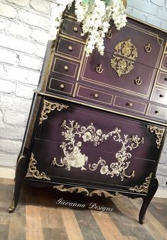 an ornate dresser with flowers on top is painted purple and gold, along with white hydrangeas