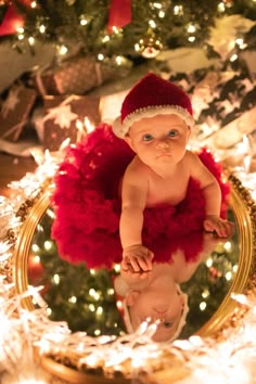 a baby wearing a santa hat and red tutu in front of a christmas tree