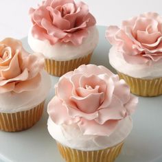 four cupcakes with pink frosting and flowers on them sitting on a plate