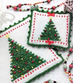 three cross stitch christmas tree coasters on a white tablecloth with beaded decorations