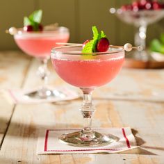 two glasses filled with pink liquid and garnished with cherries on a wooden table