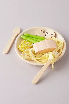 a plate with pasta, meat and vegetables on it next to two wooden spoons