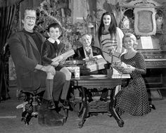 a group of people sitting around a table in front of a piano and christmas tree