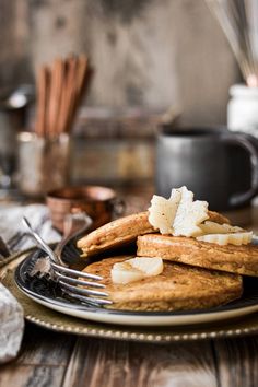 a plate topped with pancakes and butter on top of a wooden table next to utensils