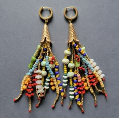 two pairs of colorful beaded earrings hanging from gold hooks on a gray surface,