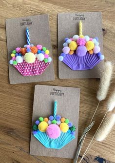 three birthday cupcakes with candles and pom - poms on them