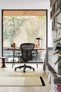 an office with a desk, chair and bookshelf in front of a window