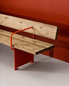 a wooden bench with an orange metal armrest on it's side against a red wall