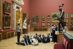 a group of children sitting on the floor in front of a statue and people standing around