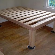 a wooden bed frame sitting on top of a hard wood floor next to a window