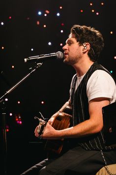 a man sitting in front of a microphone while holding a guitar and singing into a microphone